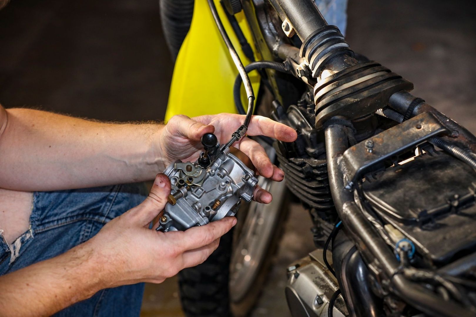 Handen houden een carburateur naast de motor van een terreinmotor